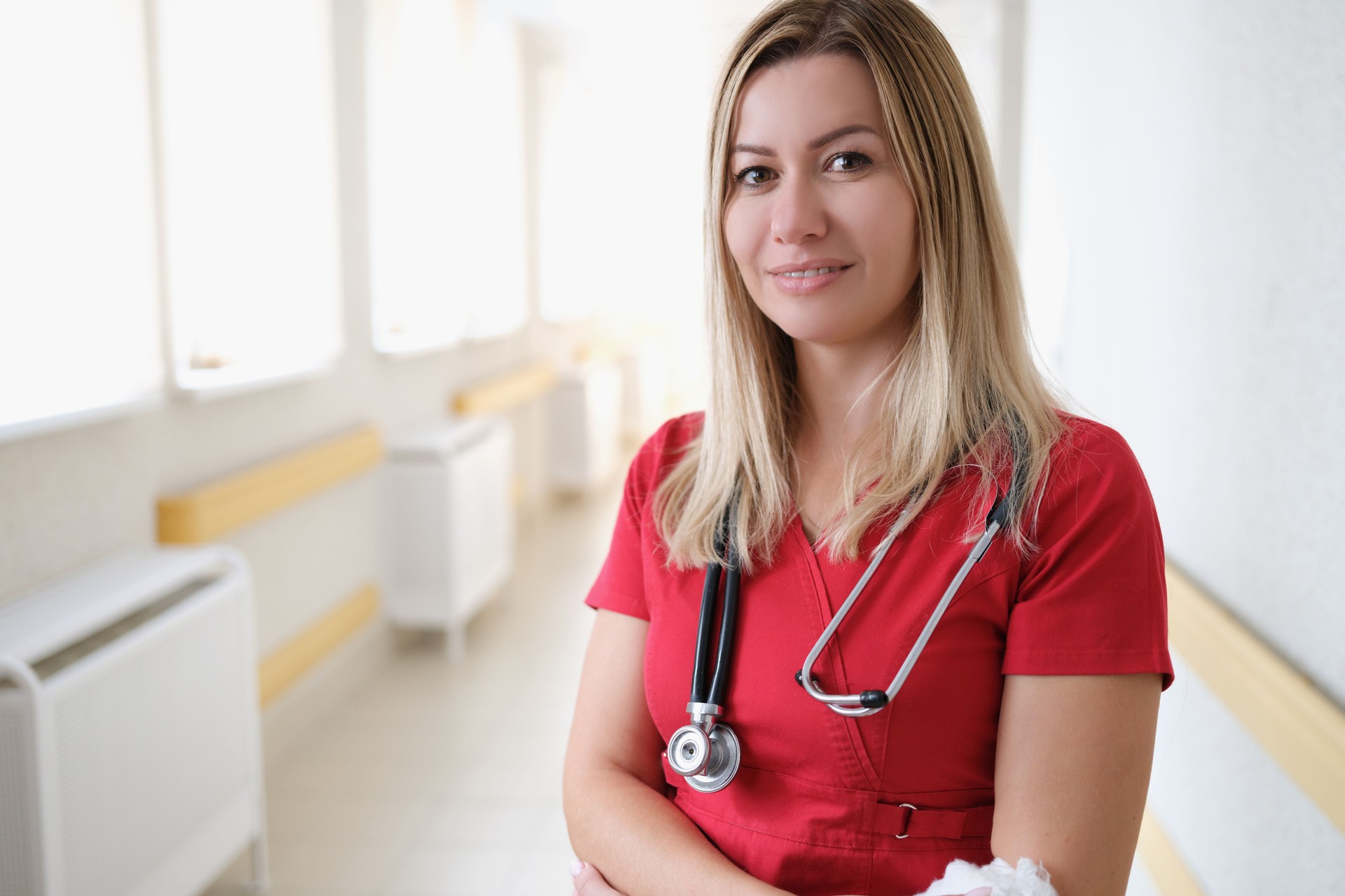 Portrait of young female doctor with stethoscope in red uniform in hospital corridor