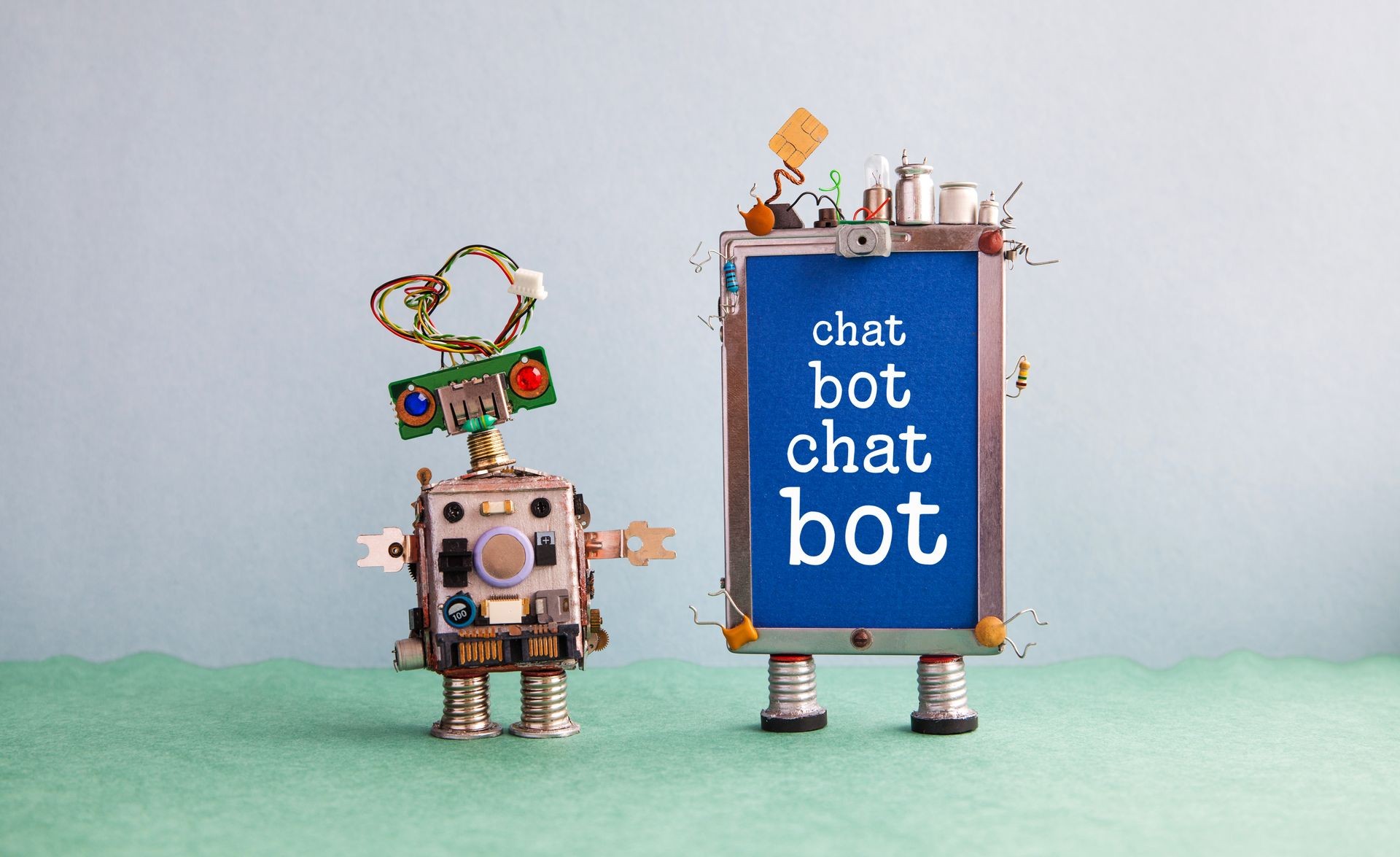 Chatbot artificial intelligence poster. Creative design robot and smartphone gadget with message Chat Bot on blue screen. Modern electronic marketing communication concept. Gray wall green floor 